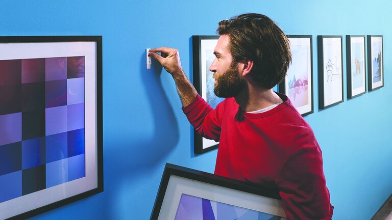 Mand hænger billede op på væggen med klæbesøm