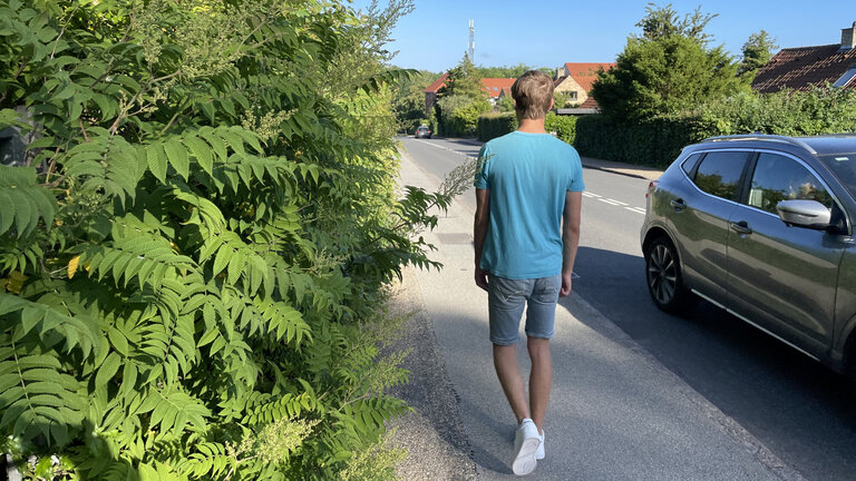 Mand går forbi uklippet hæk