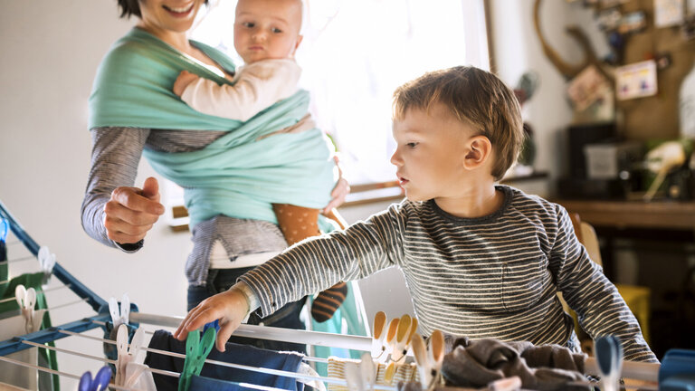 Mor med baby og lille dreng tørrer tøj på tørrestativ i bolig