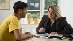 Bankrådgiver og kunde sidder ved bord og taler sammen.