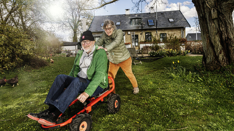 Lise Palm skubber sin mand, Peter Aalbæk Jensen, på en mooncar, med deres hus i baggrunden.